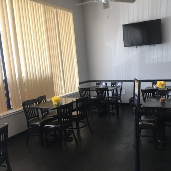 Interior of The Hunger Tamer restaurant with dark tables and chairs, light walls, and window blinds.