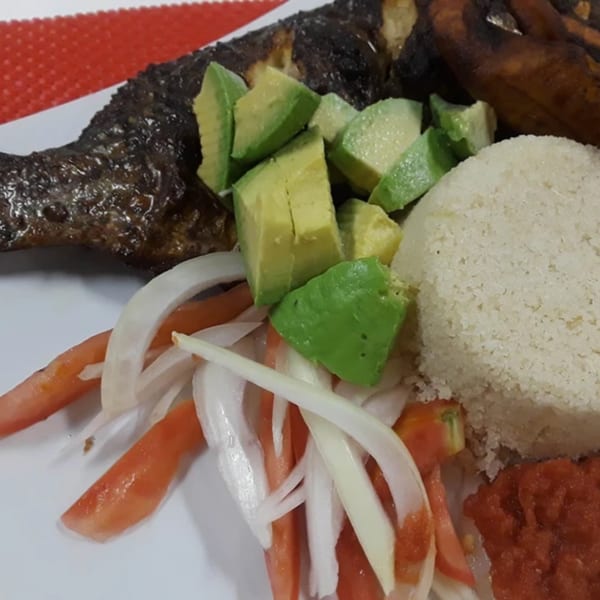African grilled fish with avocado, rice, tomato, onion, and red sauce on a white plate.