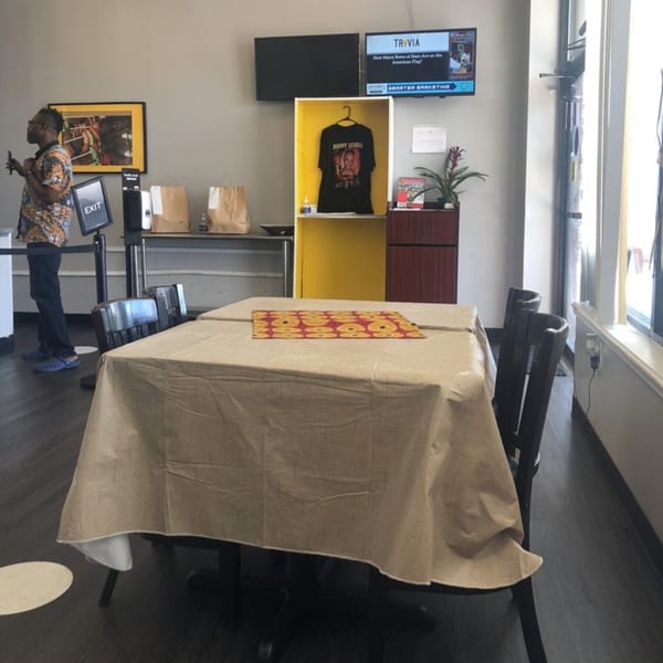 Interior of The Hunger Tamer restaurant with a table, chairs, and a person standing near an exit sign.