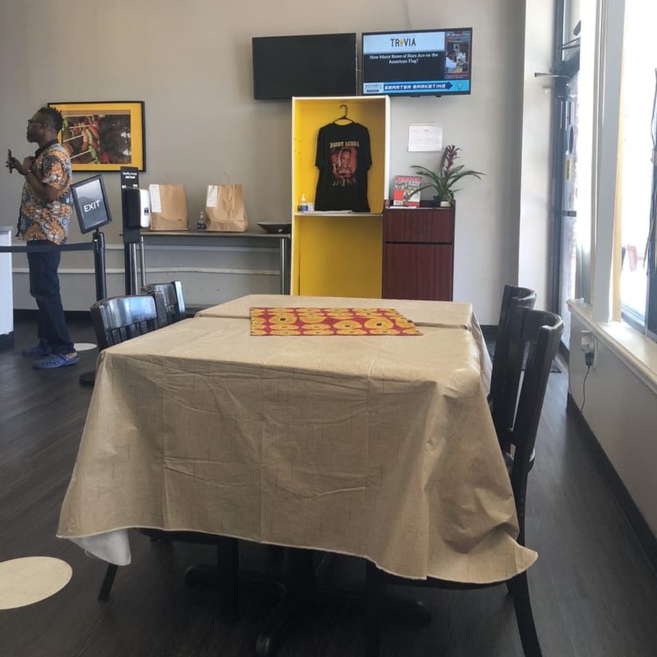 Interior of The Hunger Tamer restaurant with a table, chairs, and a person standing near an exit sign.