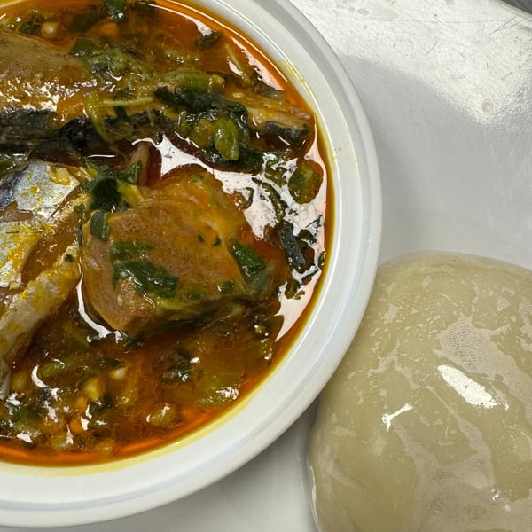 A bowl of African okra soup with fish and a side of fufu on a white surface.