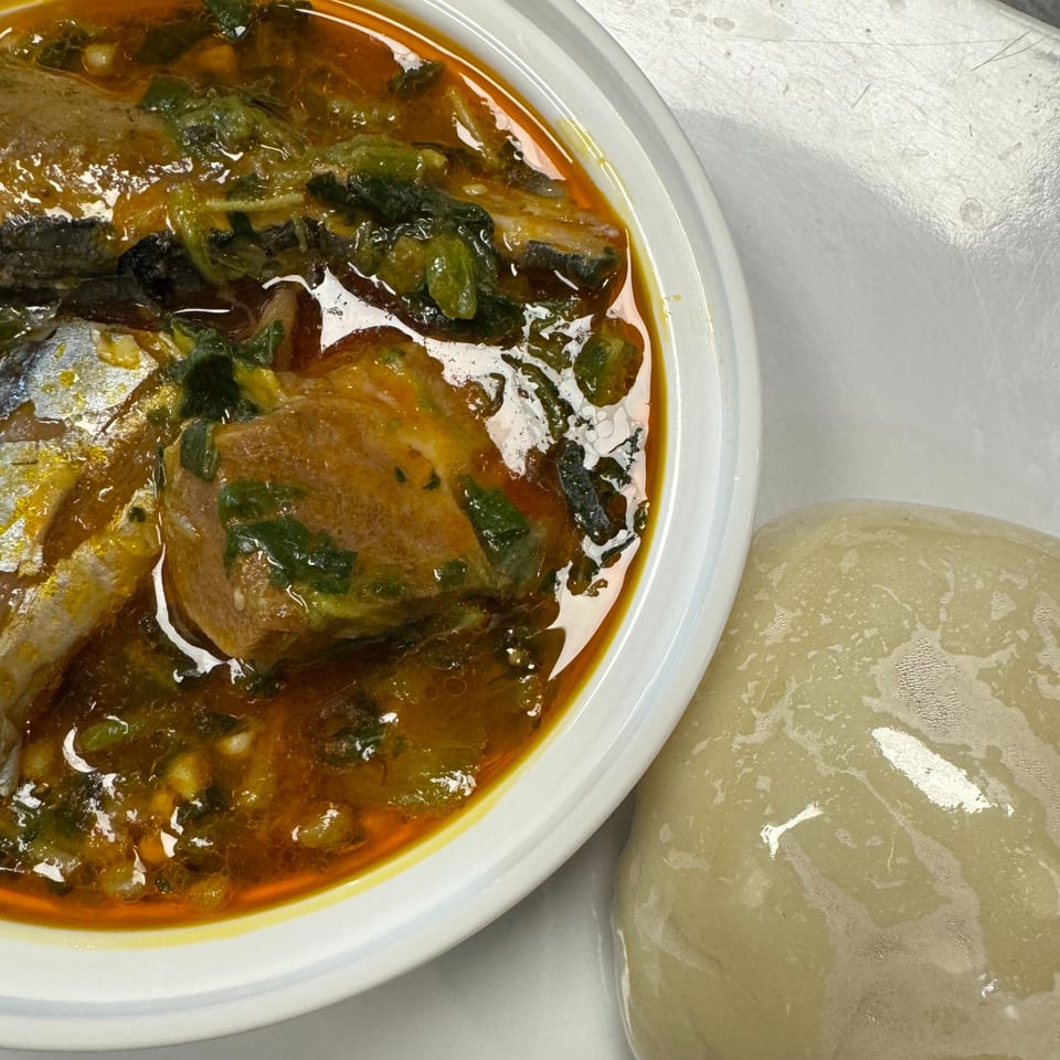 A bowl of African okra soup with fish and a side of fufu on a white surface.