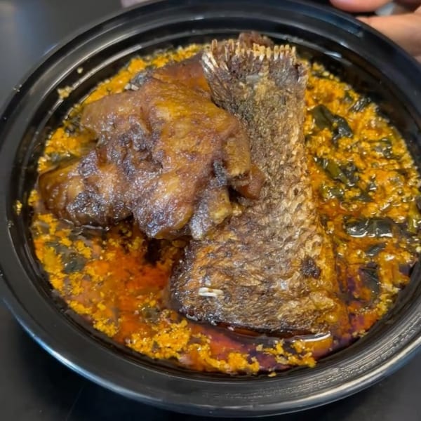 African dish with a large piece of fried fish and a smaller piece of meat in a rich, orange-yellow sauce.