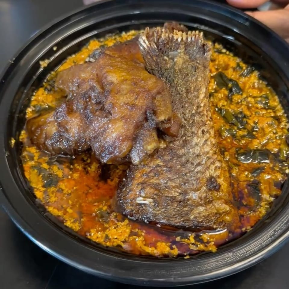 African dish with a large piece of fried fish and a smaller piece of meat in a rich, orange-yellow sauce.