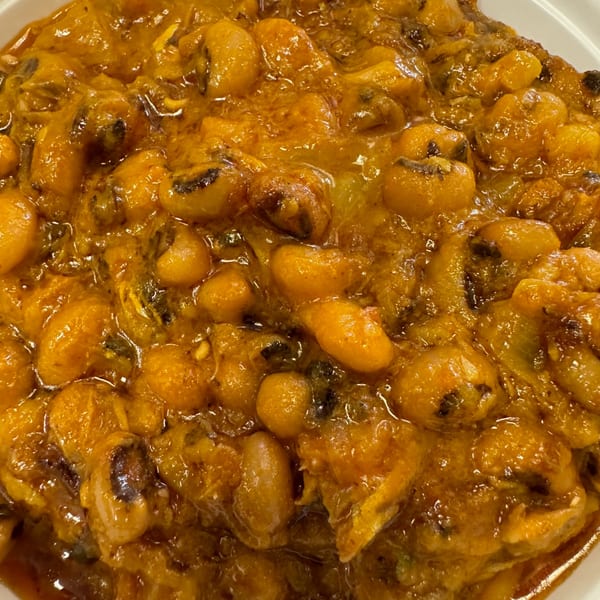 Close-up of a rich, orange-brown African stew with beans and other ingredients in a white bowl.