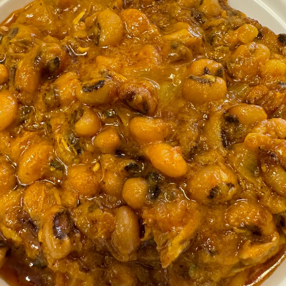 Close-up of a rich, orange-brown African stew with beans and other ingredients in a white bowl.