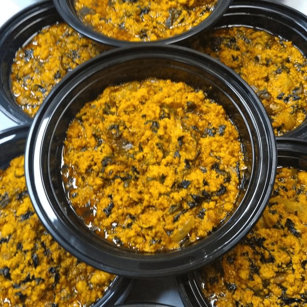 Multiple black containers filled with vibrant yellow African stew, featuring dark green leafy vegetables.