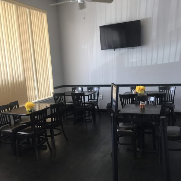 Interior of The Hunger Tamer restaurant with dark tables and chairs, light walls, and a TV.